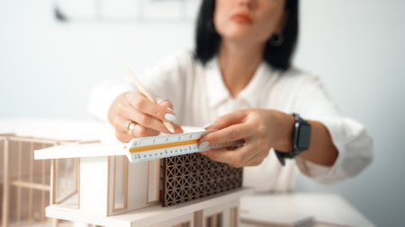 Closeup portrait image of professional young beautiful engineer architect using triangular scale measures house model with focusing at modern office. Business creative design concept. Immaculate.の写真素材