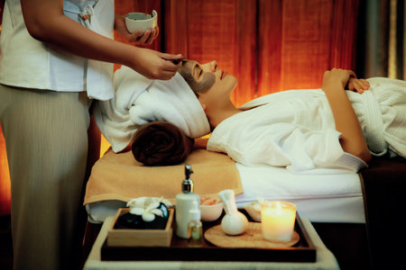 Spa salon composition set up table on blurred background of woman customer in rejuvenating by luxurious face cream massage with warm lighting candle. Facial skin treatment and beauty care. Quiescentの写真素材