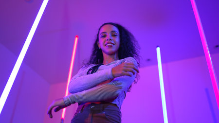 Low angle camera of hispanic dancer looking at camera and dancing to city pop music. Professional attractive hipster moving to hip hop song with purple led or neon light. Stylish cloth. Regalement.の写真素材