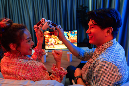 Couple gamer with hands cross of joystick playing fighting video game with winner together on tv...