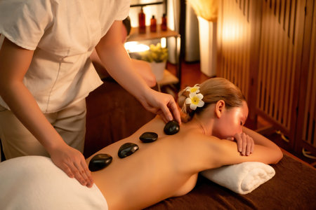 Hot stone massage at spa salon in luxury resort with warm candle light, blissful woman customer enjoying spa basalt stone massage glide over body with soothing warmth. Quiescentの写真素材