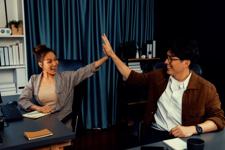Successful smiling business partners earning high revenue in sales taking high five in creative design architecture planning project job investment via email at modern home office at night. Infobahn.の写真素材