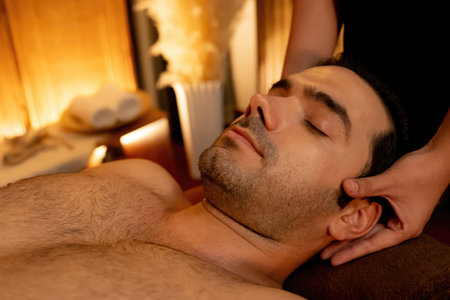 Caucasian man enjoying relaxing anti-stress head massage and pampering facial beauty skin recreation leisure in warm candle lighting ambient salon spa in luxury resort or hotel. Quiescentの写真素材