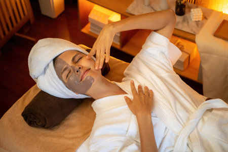 Serene ambiance of spa salon, top view woman customer indulges in rejuvenating with charcoal face cream massage with warm lighting candle. Facial skin treatment and beauty care concept. Quiescentの写真素材