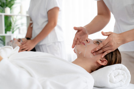 Serene modern daylight ambiance of spa salon, couple customer indulges in rejuvenating with facial skincare mask. Facial skin treatment and beauty cosmetology procedure for face. Quiescentの写真素材