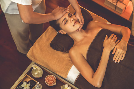 Caucasian woman enjoying relaxing anti-stress head massage and pampering facial beauty skin recreation leisure in warm candle lighting ambient salon spa in luxury resort or hotel. Quiescentの写真素材