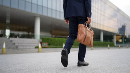 Closeup of skilled business man leg walking while holding bag. Cropped image of project manager focus on leg. Traveling, moving, journey, getting a new position, job changing. Back view. Exultant.の写真素材