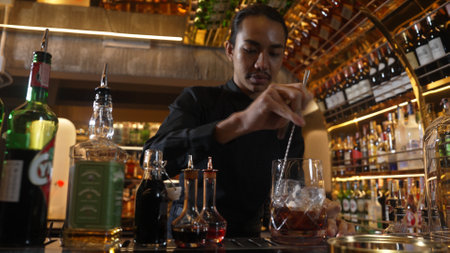 Smart Asian bartender using stirring mixed alcohol syrup into glass with ice for on the rock served mixing looking camera zoom out special refresh cocktail nightlife mixology at nightclub. Vinosity.のeditorial素材