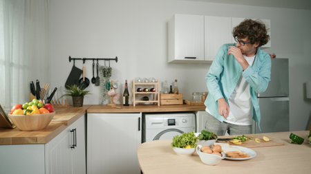 Happy father moves to music while cooking food and preparing lunch at modern kitchen. Active dad dancing to song while making healthy food or salad surrounded with vegetables and kitchenware.の写真素材