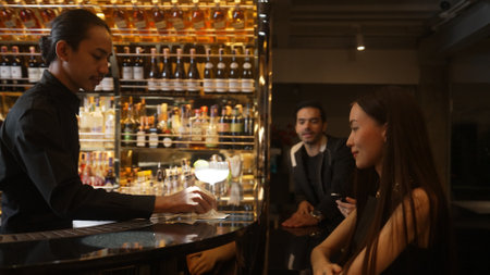 Bartender preparing vodka cocktail garnished with slice lemonade serving customer or couple on...