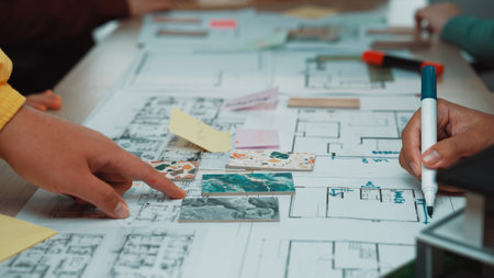 Engaging team planning session featuring hands pointing at an architectural layout with sketches and...