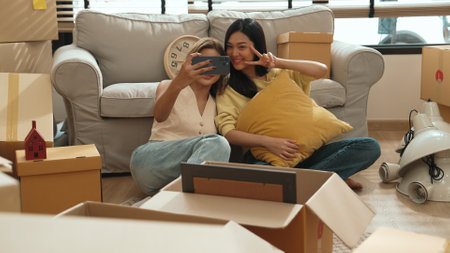 Girl taking a photo while sitting at living room in moving day. Couple spending time together while lying at sofa surrounded with cardboard box. Relocation and relationship.の写真素材