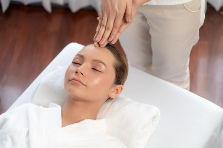Caucasian woman enjoying relaxing anti-stress head massage and pampering facial beauty skin recreation leisure in dayspa modern light ambient at luxury resort or hotel spa salon. Quiescentの写真素材