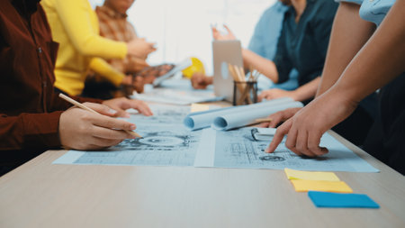 A group of professionals engaged in a collaborative planning session, discussing charts and blueprints on a modern workspace table to foster creativity and innovation.の写真素材