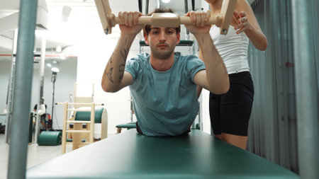 Client practicing a bar-based exercise on Pilates Cadillac with instructor guidance. Male student...