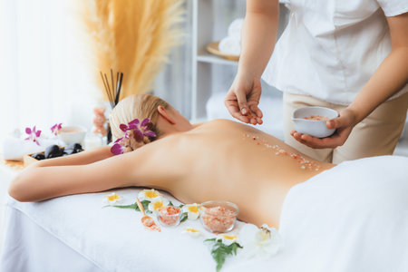 Woman customer having exfoliation treatment in luxury spa salon with warmth candle light ambient. Salt scrub beauty treatment in health spa body scrub. Quiescentの写真素材