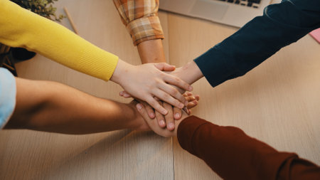 A diverse group of individuals showcases teamwork by placing their hands together in a gesture of...