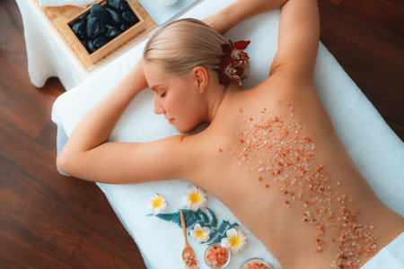 Panorama top view woman customer having exfoliation treatment in luxury spa salon with warmth candle light ambient. Salt scrub beauty treatment in health spa body scrub. Quiescentの写真素材