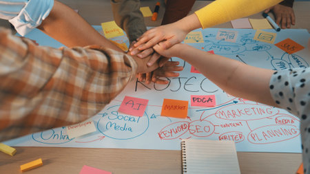 Enthusiastic teamwork is depicted as diverse hands unite over a detailed brainstorming sheet filled...