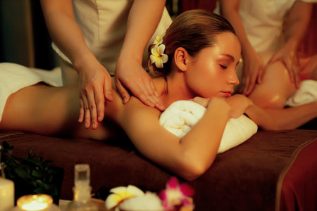 Caucasian couple customer enjoying relaxing anti-stress spa massage and pampering with beauty skin recreation leisure in warm candle lighting ambient salon spa at luxury resort or hotel. Quiescentの写真素材
