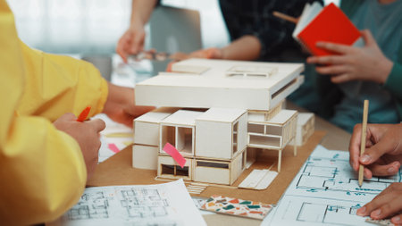 A dynamic architectural design session where a diverse group of designers collaborate around a model and blueprints, sharing ideas and creativity.の写真素材