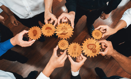 A diverse group of professionals collaboratively holds wooden gears symbolizing ethics, justice, and innovation, showcasing teamwork in business decision-making and growth strategies.の写真素材