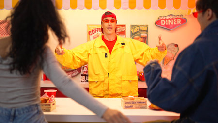 Attractive restaurant worker picking cherry and giving it to multicultural customer. Professional man moving to freestyle music or dancing along song while give cherry for diverse group. Regalement.のeditorial素材