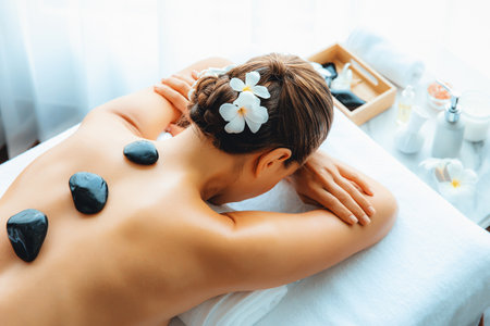 Hot stone massage at spa salon in luxury resort with day light serenity ambient, blissful woman customer enjoying spa basalt stone massage glide over body with soothing warmth. Quiescentの写真素材