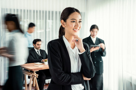 Portrait of happy young asian businesswoman looking at camera with motion blur background of business people movement in dynamic business meeting.の写真素材