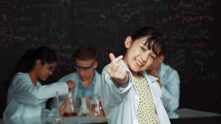 Asian scientist show to camera while diverse group doing experiment. Young schoolgirl standing at blackboard with chemical theory written while wearing lab coat at laboratory.の写真素材