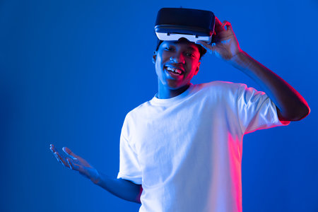 Surprised young African American looking through VR holding interesting object hologram on pink blue...
