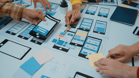 A group of professionals engages in a creative session, collaborating on mobile app wireframes and...