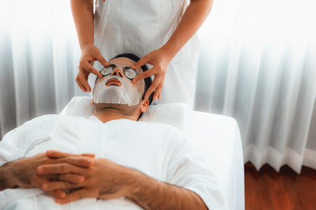 Serene daylight ambiance of spa salon, man customer indulges in rejuvenating with luxurious cucumber facial mask. Facial skincare treatment and beauty care concept. Quiescentの写真素材
