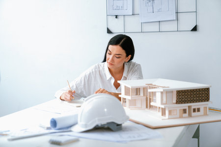 Closeup image of young architect engineer writing house structure in blueprint with document and...
