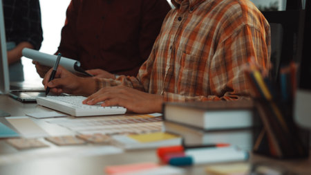 A professional designer is engaged in a digital project at a modern desk, surrounded by papers, colorful markers, and a collaborative team, fostering creativity and innovation.の写真素材