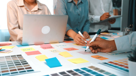 A dynamic team collaborates in a modern office environment, utilizing laptops, color palettes, and...