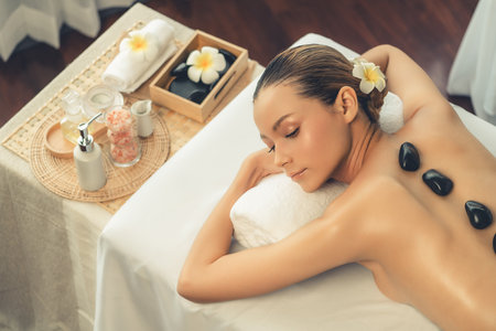 Hot stone massage at spa salon in luxury resort with day light serenity ambient, blissful woman customer enjoying spa basalt stone massage glide over body with soothing warmth. Quiescentの写真素材