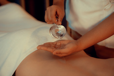 Closeup masseur hand pouring aroma oil on woman back. Masseuse prepare oil massage procedure for customer at spa salon in luxury resort. Aroma oil body massage therapy concept. Quiescentの写真素材