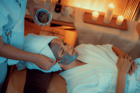 Serene ambiance of spa salon, woman customer indulges in rejuvenating with charcoal face cream massage with warm lighting candle. Facial skin treatment and beauty care concept. Quiescentの写真素材