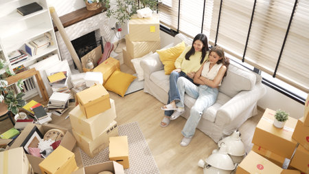 Top view of young girl invited cheerful friend sitting near her at moving day. Couple of happy woman...