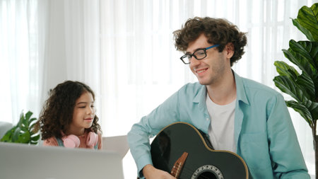 Caucasian dad plays guitar and moves to music while daughter waves and dances to an acoustic song. Happy family spends time together at home. Creative activity concept. Lifestyle. Pedagogy.の写真素材