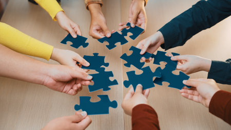 Diverse hands reach out to assemble blue puzzle pieces on a wooden table, symbolizing teamwork and collaboration during a creative brainstorming session.の写真素材