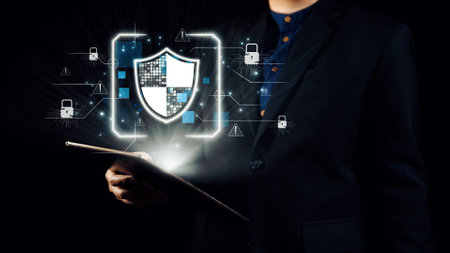 A professional man holds a tablet against a dark background with digital security elements. The glowing shield symbol highlights the importance of data protection and management. Qubitの写真素材
