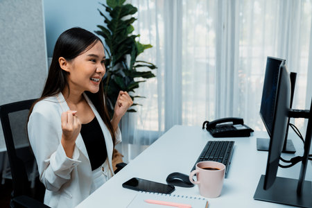 Successful young Asian businesswoman earning highest profit with fist up in exchange stock market on dynamic business graph on pc screens at modern office, analyzing financial technology. Stratagem.の写真素材