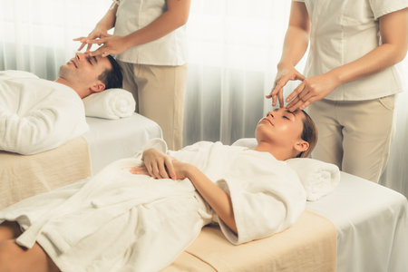 Caucasian couple enjoying relaxing anti-stress head massage and pampering facial beauty skin recreation leisure in dayspa modern light ambient at luxury resort or hotel spa salon. Quiescentの写真素材
