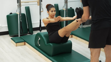 Happy pilates instructor guiding a client in a core-strengthening exercise using arc barrel...