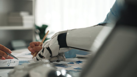 Human and Robot Collaboration in Modern Workplace with Analytics on Desk, Focus on Robotic Arm and Human Interaction in Digital Environment.の写真素材