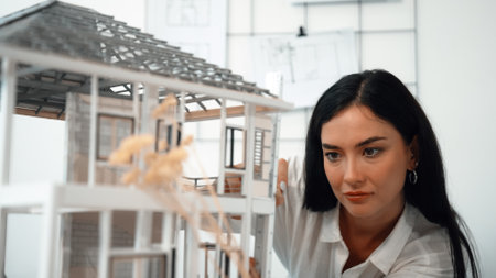 Young beautiful caucasian architect engineer turns house model around to inspect house construction and check mistake point to solve the problem on meeting table at modern office. Closeup. Immaculate.の写真素材