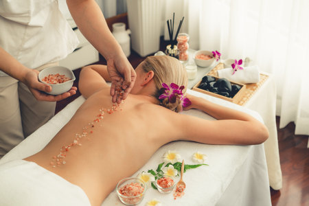 Woman customer having exfoliation treatment in luxury spa salon with warmth candle light ambient. Salt scrub beauty treatment in health spa body scrub. Quiescentの写真素材