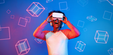 African girl with VR glasses standing at blue and pink background and looking at floating geometric shape. Excited person searching and entering visual reality world. Technology innovation. Ingenuity.の写真素材